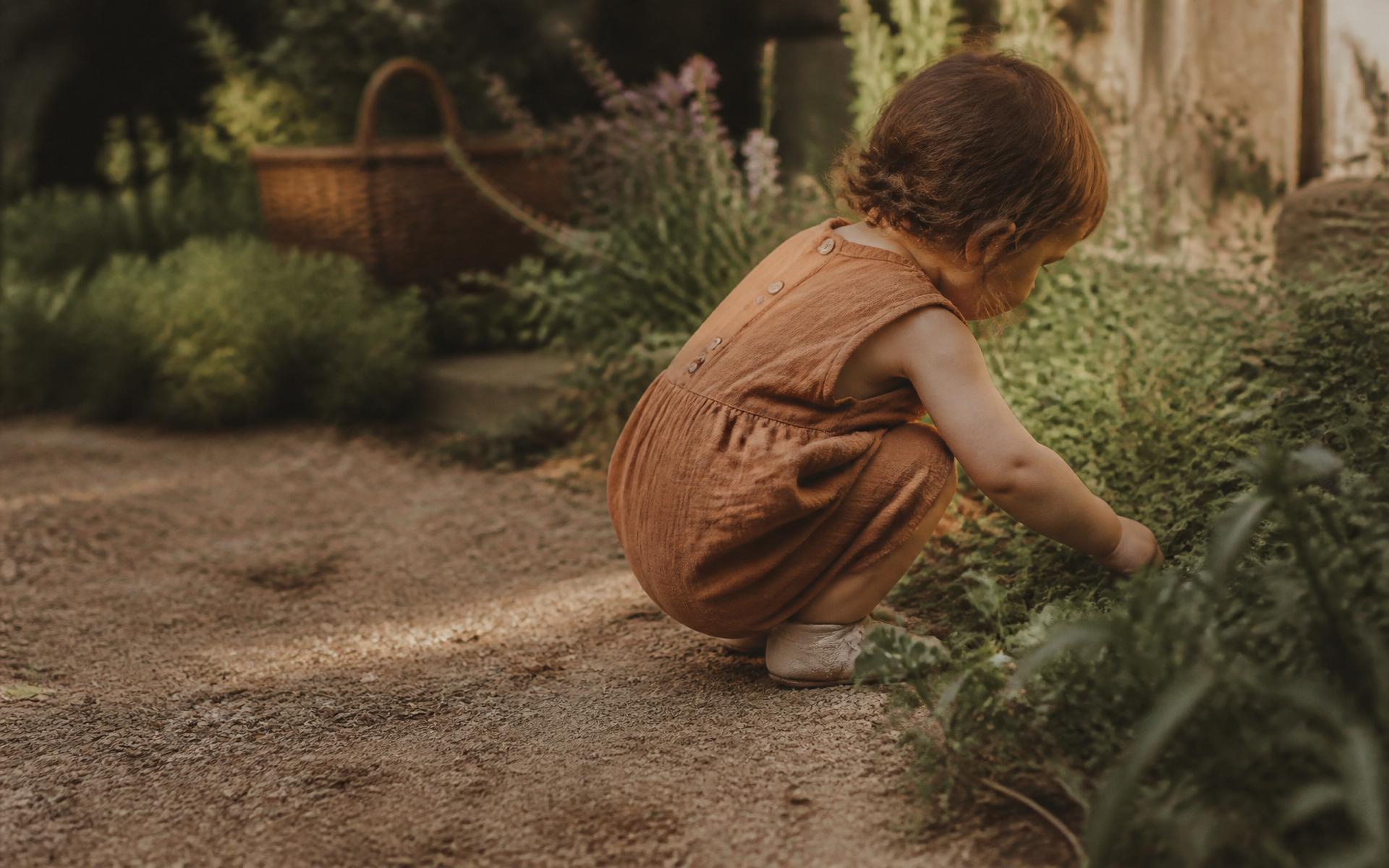 A young child laughing while playing outdoors in a leafy garden